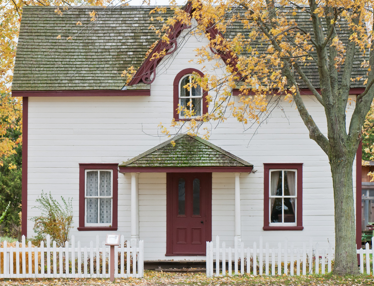 Modest home with fresh white paint and maroon trim on a pretty fall day