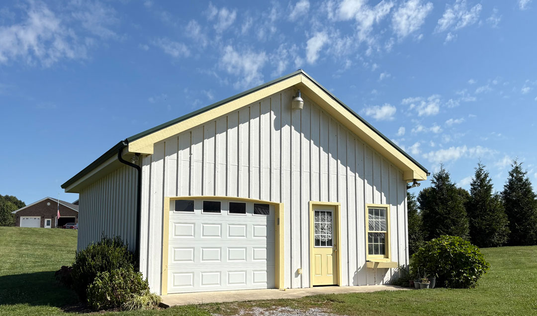Newly painted outbuilding with white board and batten siding and happy yellow trim