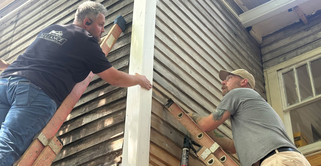Owner Wesley News and team member atop ladders reviewing details of historic preservation job